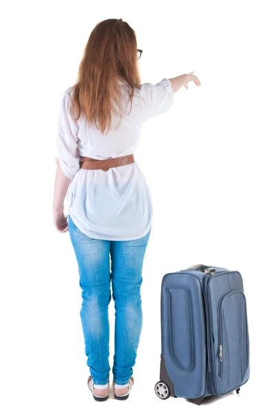 Traveling young woman with suitcas points at wall. — Stock Photo, Image