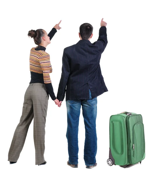 Молода пара подорожує з валізою і вказує на стіну — стокове фото