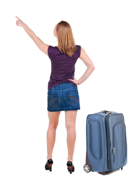 Vacker ung kvinna i klänning reser med resväska och pekar på väggen — Stockfoto