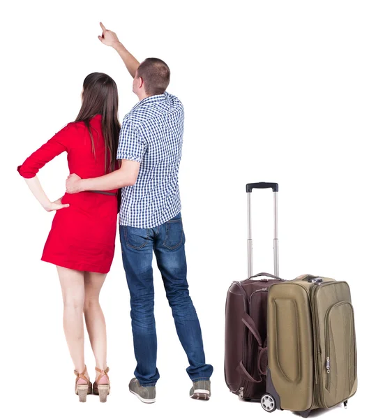Mladí manželé na cestách s kufrem a ukazovala na zeď — Stock fotografie