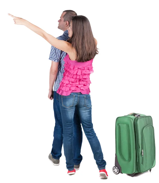 Молода пара подорожує з валізами і вказує на стіну — стокове фото