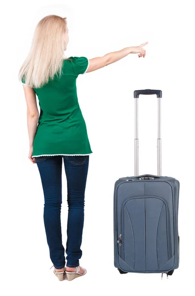 Back view of young brunette woman traveling with suitcas and pointing at wall — Stock Photo, Image