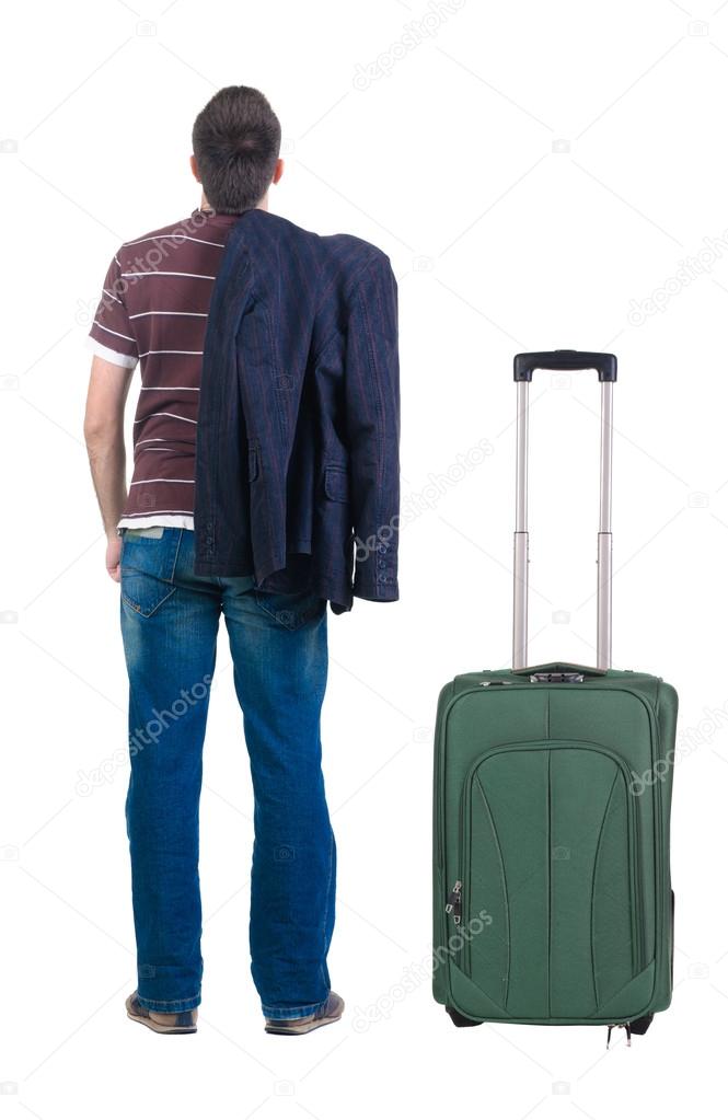 Young man traveling with suitcase looks ahead. Rear view.