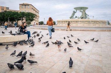 Triton çeşmesinin yanında güvercinleri besleyen kız.