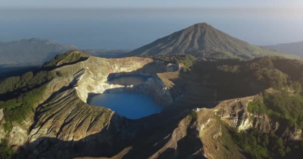 Lago da cratera do vulcão Kelimutu na Indonésia. Voo aéreo sobre a paisagem vulcânica com água azul — Vídeo de Stock