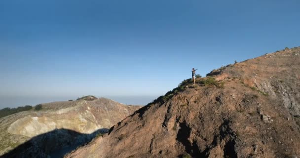 Kobieta stojąca na szczycie góry z podniesionymi rękami. Wulkan krater jezioro błękitne niebo w tle. — Wideo stockowe