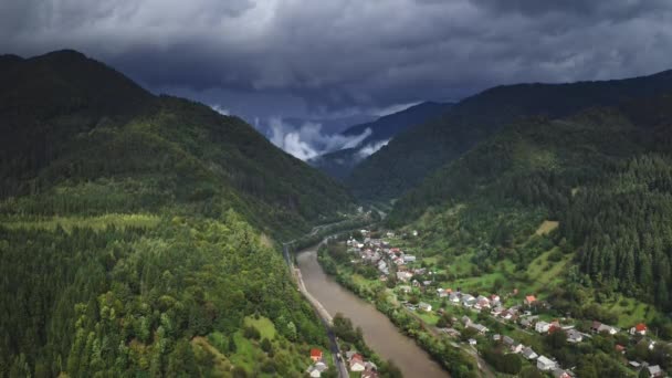 Alpes pueblo de montaña bajo nubes de tormenta cielo. Vuelo aéreo sobre casas rurales a lo largo del río — Vídeo de stock