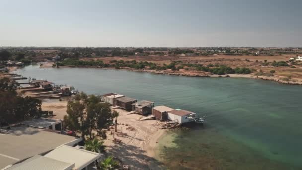 Uitzicht op de kustlijn van de rivier. Vissersdorp met boothuizen op pier. Zandstrand, houten schepen — Stockvideo