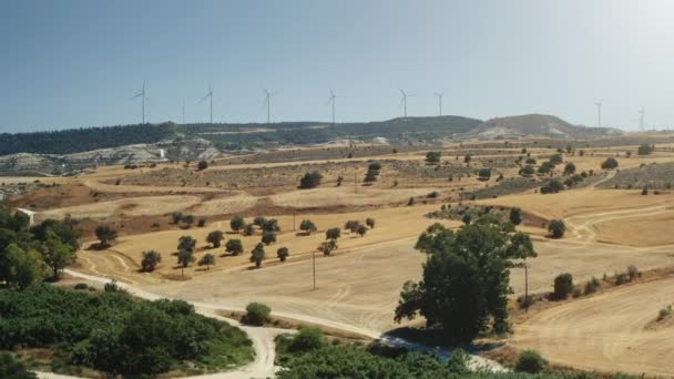 Aerial flight over dry countryside landscape with wind mill plant in the background. Modern wind turbines — Stock Video