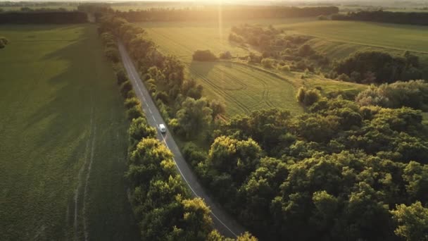 Pôr do sol estrada paisagem natureza aérea. Carro branco andando estrada de asfalto rural em raios de pôr do sol — Vídeo de Stock