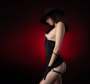 Şapkalı bir kız, ince, çıplak, siyah gecelikli, bacaklarında deri kayışlarla.