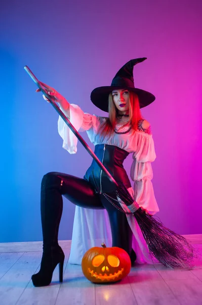 ハロウィン用の魔女の衣装を着た女の子ネオンライトのほうきとカボチャで — ストック写真