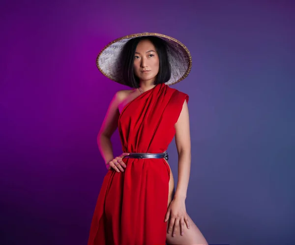 Asiático mujer en rojo capa y asiático sombrero posando en brillante neón fondo — Foto de Stock