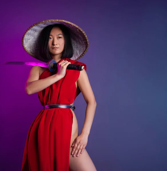 Portrait of an Asian woman in a red cape and an Asian hat with a katana in her hand image of a samurai — Stock Photo, Image
