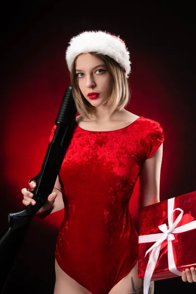 Dziewczyna w czerwonym body i kapelusz Świętego Mikołaja ze strzelbą w rękach na Boże Narodzenie — Zdjęcie stockowe