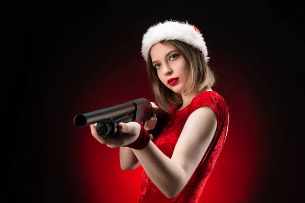 A girl in a red bodysuit and a Santa Claus hat with a shotgun in her hands for Christmas Royalty Free Stock Photos