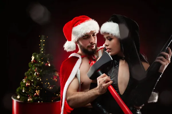 Boże Narodzenie romantyczna sesja zdjęciowa faceta i dziewczyny w Nowym Roku Santa Claus kostiumy z bronią, choinka na ciemnym czerwonym tle — Zdjęcie stockowe