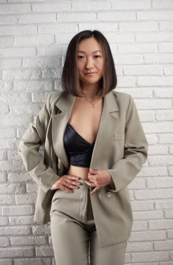 Şık takım elbiseli şık bir Asyalı kadın beyaz bir duvara karşı poz veriyor.