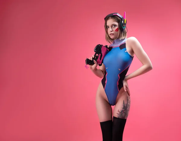 Parlak takım elbiseli seksi oyuncu kız ve pembe arka planda silahı olan bir oyun kulaklığı.