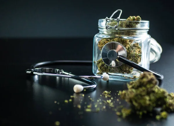 Dry medical cannabis in a jar with a stethoscope on a black background — Stock Photo, Image