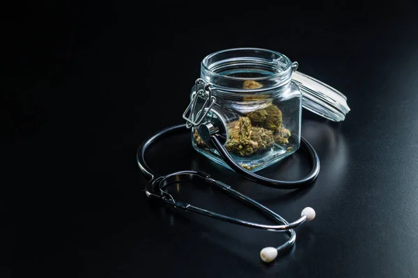 Suché lékařské konopí ve sklenici se stetoskopem na černém pozadí — Stock fotografie