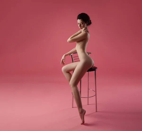Nude girl with a perfect figure on a bar stool with a pink background — Stock Photo, Image