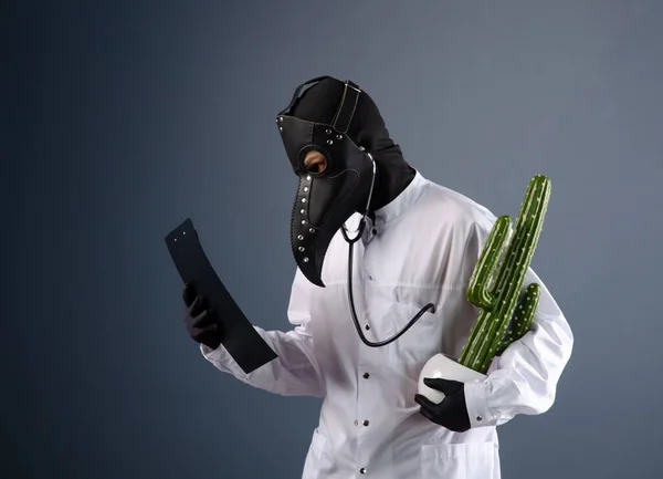 Un médico con una bata, con una máscara de médico plaga con un cactus en las manos — Foto de Stock
