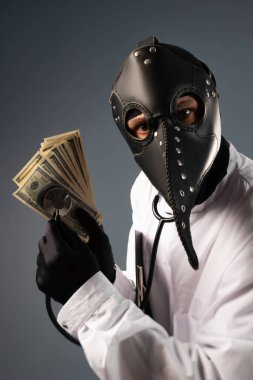 a corrupt doctor in a bathrobe and a plague doctor mask with a wad of money in his hands