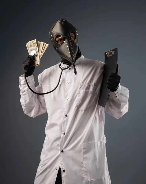 Ένας διεφθαρμένος γιατρός με μπουρνούζι και μάσκα γιατρού πανούκλας με ένα μάτσο λεφτά στα χέρια του. — Φωτογραφία Αρχείου