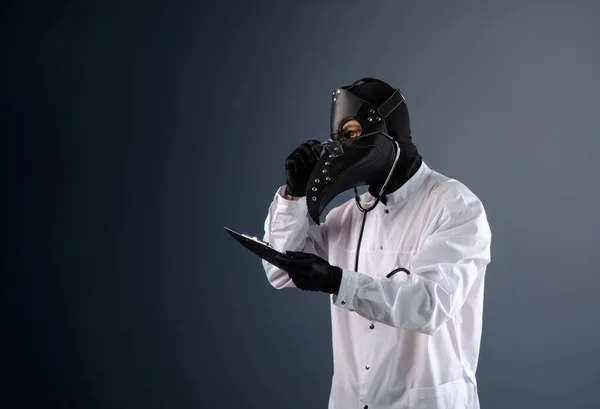 Un médico con una bata con una máscara de médico de la peste con un estetoscopio en las manos — Foto de Stock
