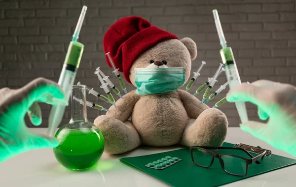Плюшевого ведмедя в медичній масці з шприцами в плечі на столі лікарів дають другу щеплення проти коронавірусу — стокове фото