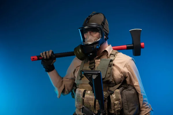 Mężczyzna w wojskowych ciuchach i masce gazowej z czerwonym toporem na ramieniu. — Zdjęcie stockowe