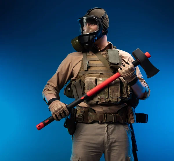 Um soldado em roupas militares com um colete à prova de bala em uma máscara de gás segura um machado de fogo vermelho em suas mãos — Fotografia de Stock