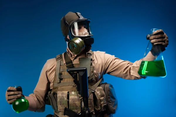 Человек в военной одежде и противогаз с лабораторными химическими колбами — стоковое фото