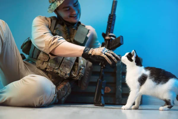 一名身穿迷彩服的男性士兵正坐在地板上，身边拿着一盒装有武器的弹药，抚摸着一只猫 — 图库照片