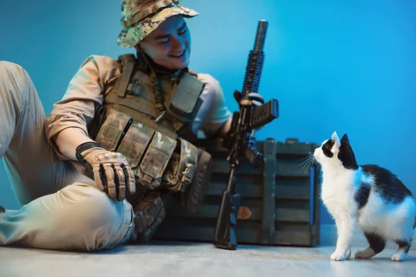 Чоловічий солдат у камуфляжі сидить на підлозі біля коробки боєприпасів зі зброєю поруч з маленьким котом — стокове фото