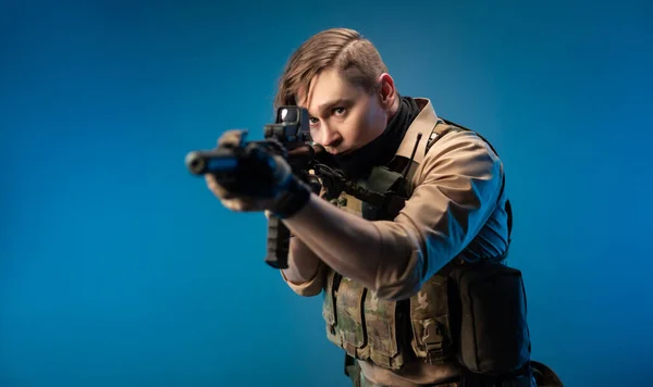 파란색 배경에 자동소총이 달린 방탄조끼를 입고 있는 남성 특수 요원 — 스톡 사진