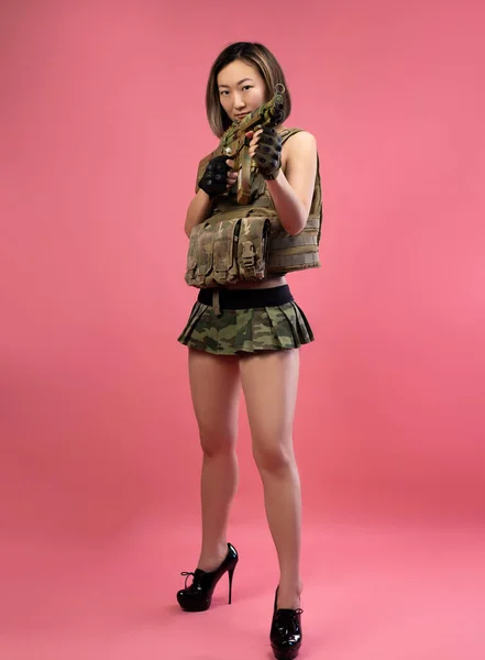 Sexy mujer asiática en ropa militar con un rifle automático en sus manos sobre un fondo rosa — Foto de Stock