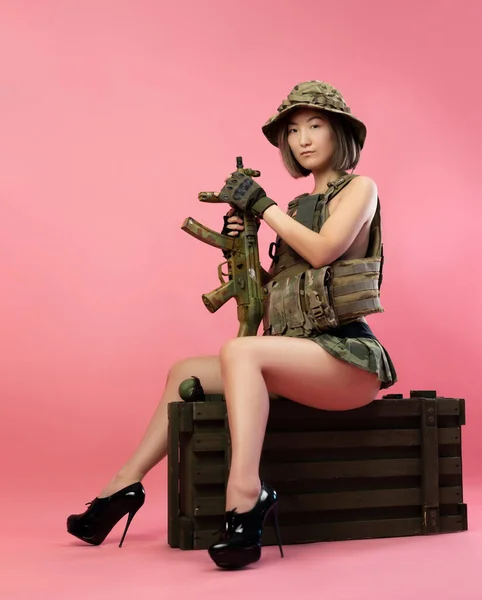 Сексуальная азиатка в военной форме с автоматом сидит на ящике с боеприпасами — стоковое фото