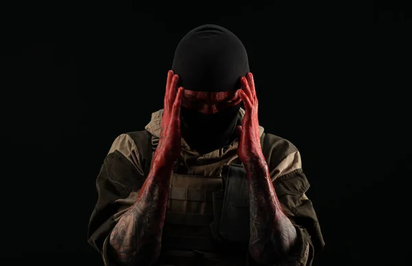 Foto de um homem com um uniforme militar e balaclava com um rosto sangrento e mãos até o cotovelo em sangue em um fundo preto — Fotografia de Stock