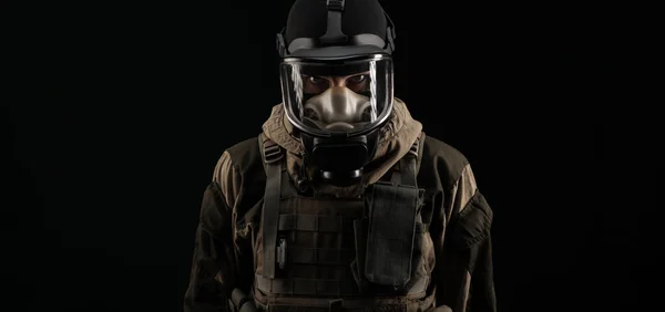 Um homem em um uniforme militar e uma máscara de gás mantém com uma expressão irritada de emoções em um fundo preto — Fotografia de Stock