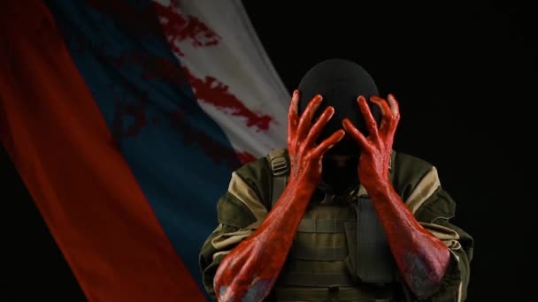 Żołnierz z zakrwawionymi rękami na tle rosyjskiej flagi trzyma głowę w szoku — Wideo stockowe