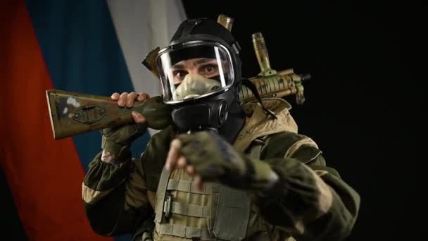 Egy dühös orosz katona az orosz zászló hátterében egy gázálarcos fegyverrel egy terrorista szerepében. — Stock videók
