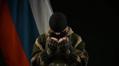 Rus bayrağının arka planında kar maskeli bir Rus askeri pişman olur ve dua eder.
