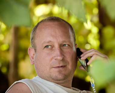 adam bir çardak twined üzüm oturan telefonla konuşuyor.