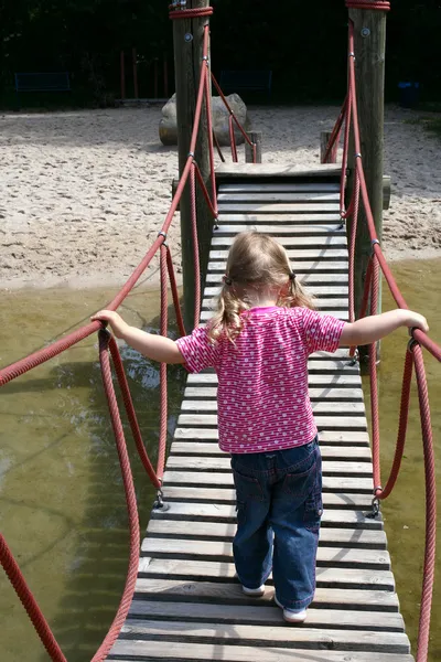 Κοριτσάκι περπάτημα σε αιωρούμενα ξύλινη γέφυρα — Stockfoto