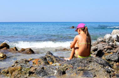 # Deniz kenarındaki bir kayanın üzerinde oturan kız #