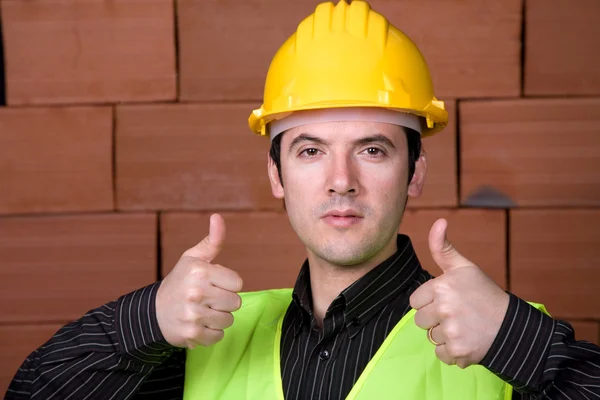 Ingenieur met gele hoed en een bakstenen muur als achtergrond — Stockfoto