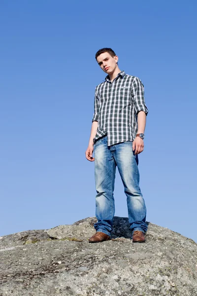 Young casual man on top of a rock with the sky as background — Stock Photo, Image