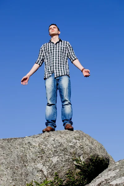 Young casual man on top of a rock with the sky as background — Stock Photo, Image